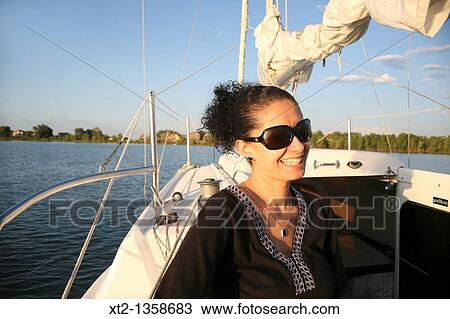 Stock Image - A beautiful young hispanic woman sits on a sailboat enjoying an evening cruise. Fotosearch