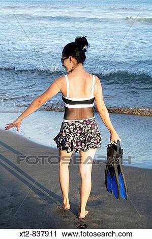 Stock Image - A beautiful young woman on the beach carrying fins walking towards the ocean in Mexico. Fotosearch