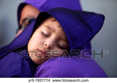 Picture - A boy dressed as a penitent sleeps in her father shoulder at the Jesus Nazareno del Perdon procession during Easter Holy Week in Antigua Guatemala, Guatemala, March 28, 2013.. Fotosearch