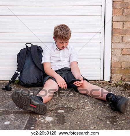 Stock Photograph - A boy of 10 looking sad and depressed in his school uniform as he looks at his mobile phone showing the effects of bullying by text or social networking in the Uk.. Fotosearch