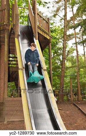 Stock Image - A boy on a slide showing movement at Bewilderwood adventure park in Hoveton, Norfolk, England, Great Britain, Uk. Fotosearch