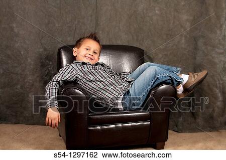 A boy sitting on a small leather chair, smiling View Large Photo Image Stock Image - A boy sitting on a small leather chair, smiling. Fotosearch