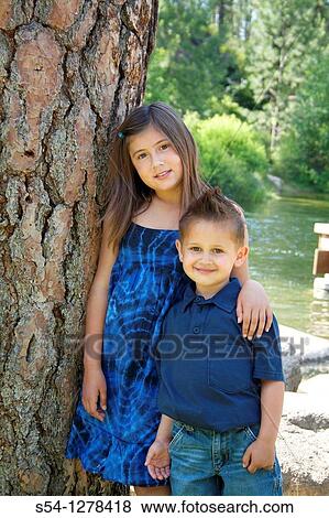 Stock Photo - A brother and sister standing together by a tree. Fotosearch