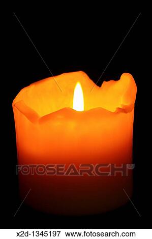 Stock Photo - A burning, well used candle with ragged melting edges against a dark background Isolated. Fotosearch