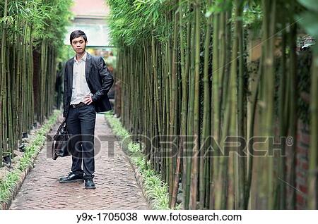 A business man dressed in a suit standing in a narrow tiled walkway lined with bamboo View Large Photo Image Stock Photo - A business man dressed in a suit standing in a narrow tiled walkway lined with bamboo. Fotosearch