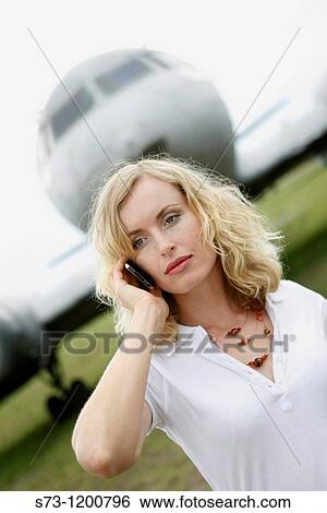 Stock Photograph - A business woman talking on a mobile phone next to a plane. Fotosearch