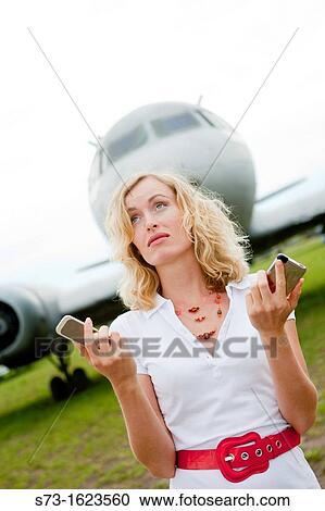 Stock Image - A business woman with two mobiles phones next to a plane. Fotosearch