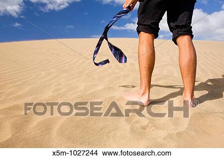 A businessman with his trousers pulled up and his tie in his hand, walking up a sand dune View Large Photo Image Picture - A businessman with his trousers pulled up and his tie in his hand, walking up a sand dune. Fotosearch