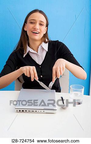 Picture - a businesswoman eating and using a laptop. Fotosearch
