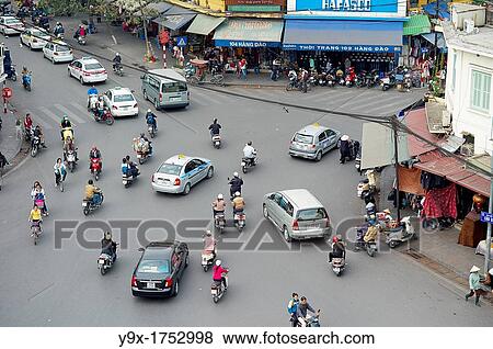 Stock Photo - A busy intersection full of cars, trucks, scooters and people in Hanoi, Vietnam. Fotosearch