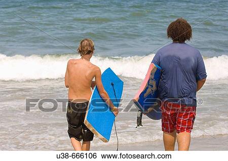 A cacausian and a Somoan boy walking into the ocean carrying boogie boards. Sandbridge Beach, Virginia Beach, Virginia, USA View Large Photo Image Stock Photograph - A cacausian and a Somoan boy walking into the ocean carrying boogie boards. Sandbridge Beach, Virginia Beach, Virginia, USA. Fotosearch