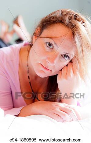 Stock Photography - A casual portrait of a 38 year old redheaded woman lying on a bed. Fotosearch
