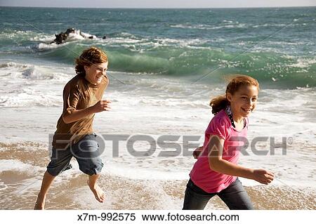 Stock Photography - A caucasian boy playfully chases a young mixed race Mexican & caucasian girl on a beach in Santa Cruz, California. Fotosearch