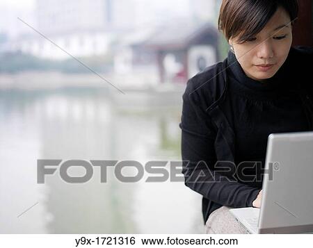 A Chinese business woman in a suit checking her email on her laptop through wireless internet with a lake and traditional Chinese architecture in the background View Large Photo Image Stock Photograph - A Chinese business woman in a suit checking her email on her laptop through wireless internet with a lake and traditional Chinese architecture in the background. Fotosearch