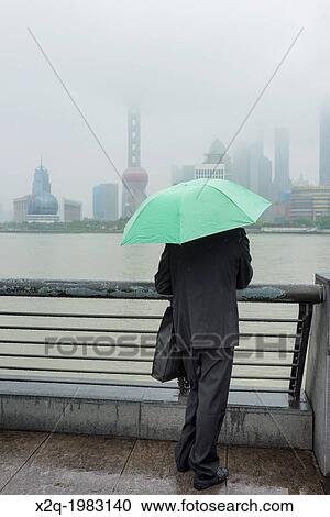 A Chinese tourist looks at the Pudong skyline from the Bund on a rainy day in Shanghai China. View Large Photo Image Stock Image - A Chinese tourist looks at the Pudong skyline from the Bund on a rainy day in Shanghai China.. Fotosearch