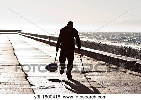 A cleaner walks along the harbour wall, slowly sweeping up rubbish left by fishermen the day before View Large Photo Image Stock Photo - A cleaner walks along the harbour wall, slowly sweeping up rubbish left by fishermen the day before. Fotosearch