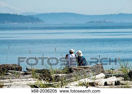 A couple sits on the beach at Island View Beach Regional Park, Saanich Peninsula, Vancouver Island, BC, Canada. View Large Photo Image Stock Photography - A couple sits on the beach at Island View Beach Regional Park, Saanich Peninsula, Vancouver Island, BC, Canada.. Fotosearch