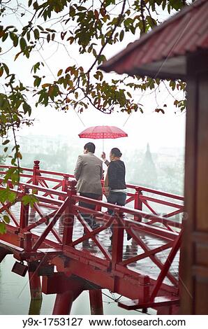 Stock Photo - A couple with a red umbrella on the red bridge at the Hoan Kiem Lake in Vietnam. Fotosearch