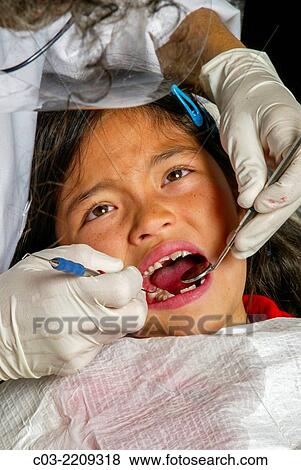 A dentist examines an Asian American girl patient's teeth in Newport Beach, CA. Note latex gloves. MODEL RELEASE. View Large Photo Image Stock Photo - A dentist examines an Asian American girl patient's teeth in Newport Beach, CA. Note latex gloves. MODEL RELEASE.. Fotosearch