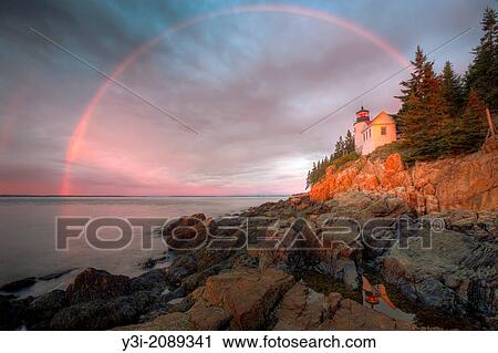 Stock Image - A double rainbow appears briefly at sunrise over Bass Harbor Head Lighthouse, which is reflected in a tidal pool as it overlooks the entrance to Bass Harbor and Blue Hill Bay in Tremont, Maine.. Fotosearch