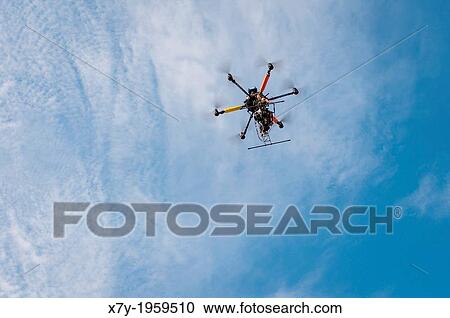 Stock Image - A drone with a camera hovers overhead in the sky.. Fotosearch