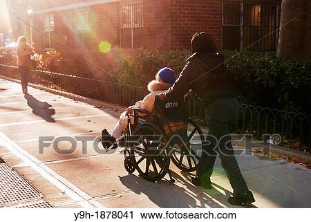A elderly woman in her wheelchair is assisted by an aide in the New York neighborhood of Chelsea View Large Photo Image Stock Image - A elderly woman in her wheelchair is assisted by an aide in the New York neighborhood of Chelsea. Fotosearch