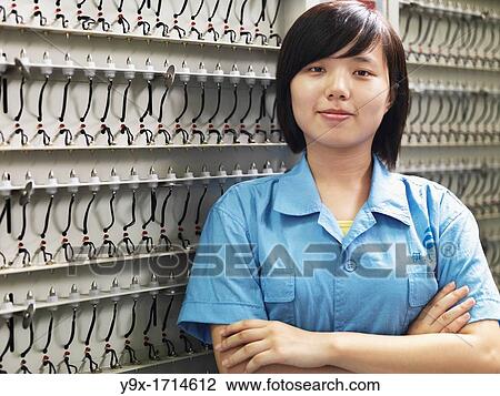 Stock Image - A factoy worker standing near a wall of plugs that verifies that the Li-Ion batteries carry a charge Shot in a Li-ion Battery Co which develops, manufactures, and markets cylindrical type rechargeable Li-ion batteries. Fotosearch