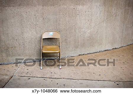 A folding chair sits against a wall View Large Photo Image Stock Photograph - A folding chair sits against a wall. Fotosearch