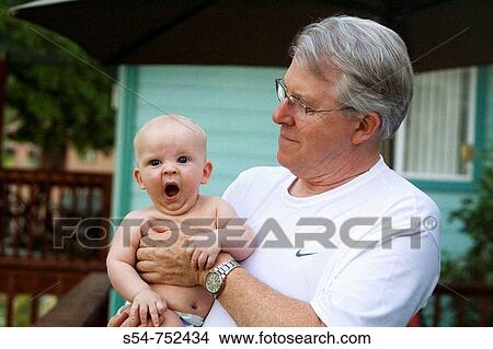 Picture - A four-month-old caucasian baby boy yawns in his grandfather's arms. Fotosearch