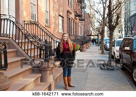 Stock Image - A girl, 16, stands on a street in front of homes in Manhattan, New York City, NY, USA. Fotosearch