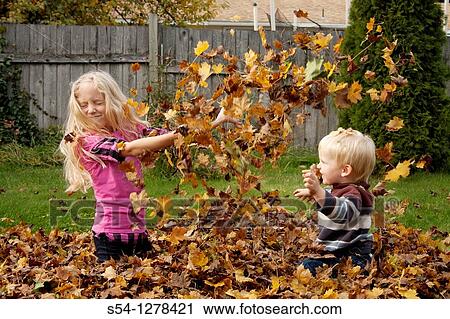 Stock Image - A girl, 5-10 and and a toddler play in a pile of leaves in the fall. Fotosearch