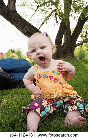 Stock Image - A girl, 7 months old, yawning and sitting in the grass at a park. Fotosearch