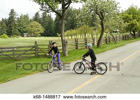 Stock Photo - a girl and boy, nine years old, on bicycles on a road on Saltspring Island, BC, Canada. Fotosearch