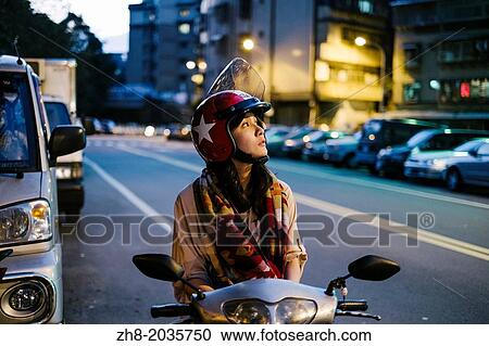 Stock Image - A girl on her scooter looks up into the evening sky in Taipei, Taiwan. Fotosearch