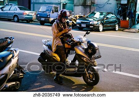 Stock Photo - A girl on her scooter text messaging on her smartphone in Taipei, Taiwan.. Fotosearch