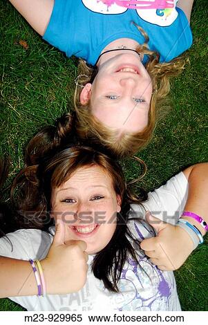A girls gives a thumb-up sign as she lies on the ground with her cousin, Pennsylvania, USA View Large Photo Image Stock Photography - A girls gives a thumb-up sign as she lies on the ground with her cousin, Pennsylvania, USA. Fotosearch