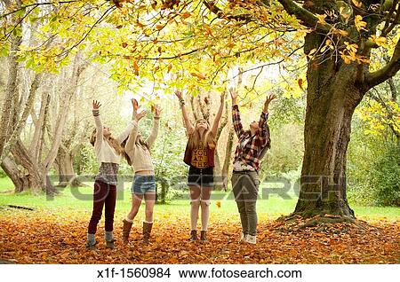 Picture - A group of 13 year old teenage girls, throwing leaves into the air, autumn morning, UK. Fotosearch