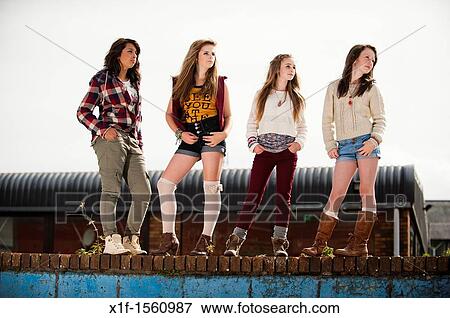 Stock Photo - A group of 13 year old teenage girls, moody with attitude standing on a wall UK. Fotosearch