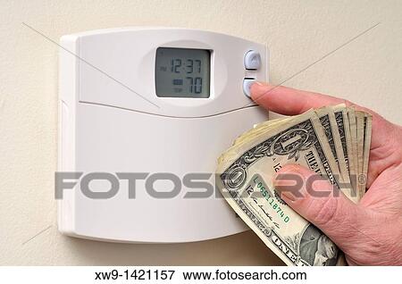 A hand clutching a some US dollar bills as it turns down the temperature setting heat thermostat View Large Photo Image Stock Photo - A hand clutching a some US dollar bills as it turns down the temperature setting heat thermostat. Fotosearch
