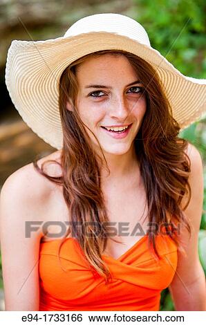 A happy 20 year old brunette woman wearing an orange top and a floppy hat in a forest setting looking directly at the camera. View Large Photo Image Stock Photograph - A happy 20 year old brunette woman wearing an orange top and a floppy hat in a forest setting looking directly at the camera.. Fotosearch
