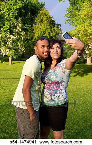 A happy, young, african-american couple outdoors, taking a picture of themselves with a cellular phone. View Large Photo Image Stock Image - A happy, young, african-american couple outdoors, taking a picture of themselves with a cellular phone.. Fotosearch