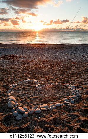 Stock Image - A heart shape made from pebbles at sunset on Aberystwyth beach wales UK. Fotosearch