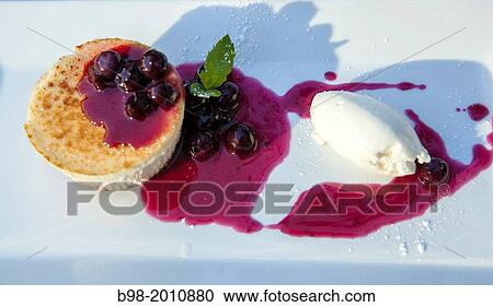 Stock Image - A high calorie dessert of creme brulee covered with a blueberry sauce, with a dollup of vanilla ice cream, in a restaurant in San Jose Caflifornia. Fotosearch