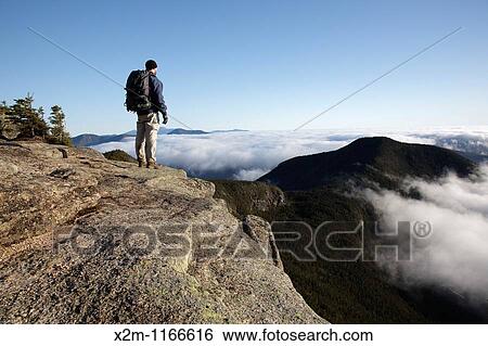 Stock Photograph - A hiker takes in the view of undercast from the summit of Mount Osceola in the White Mountains, New Hampshire USA. Fotosearch