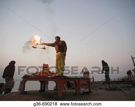 Stock Photo - A Hindu priest performs a ritual before sunrise on the bank of the Ganga river in Varanasi, India, a sacred Hindu pilgrimage site.. Fotosearch