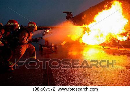 Stock Image - A hose team assigned to a ship's repair locker combats a controlled fire on the Mobile Aircraft Firefighting Training Device (MAFTD. Fotosearch
