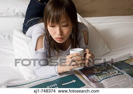 A Japanese woman resting on her hotel room bed reading a newspaper and drinking coffee. View Large Photo Image Picture - A Japanese woman resting on her hotel room bed reading a newspaper and drinking coffee.. Fotosearch