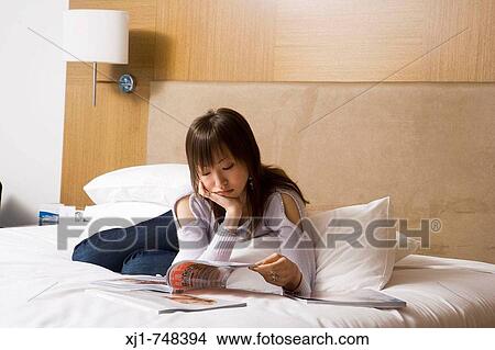 A Japanese woman resting on her hotel room bed reading a magazine View Large Photo Image Picture - A Japanese woman resting on her hotel room bed reading a magazine. Fotosearch