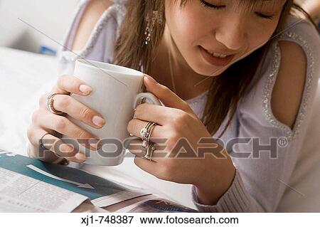 A Japanese woman resting on her hotel room bed reading a newspaper and drinking coffee. View Large Photo Image Stock Photo - A Japanese woman resting on her hotel room bed reading a newspaper and drinking coffee.. Fotosearch