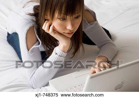 A Japanese woman sitting on a bed using a laptop computer. View Large Photo Image Stock Photography - A Japanese woman sitting on a bed using a laptop computer.. Fotosearch